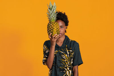 Young african american woman with short hair dressed in a summer shirt posing with pineapple