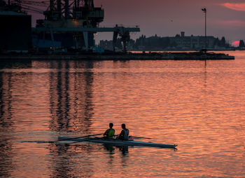 Silhouette people on boat in river against sky during sunset