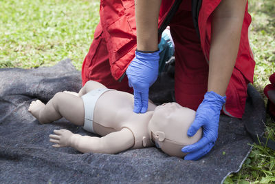 Midsection of person touching baby mannequin lying on grass field