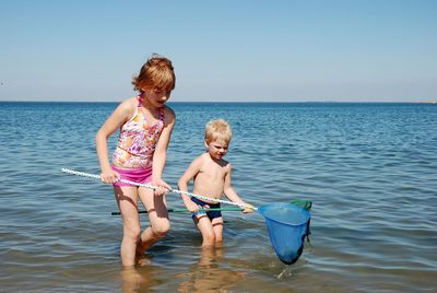 Happy friends standing in sea against clear sky