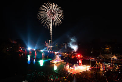 Firework display over illuminated city against sky at night