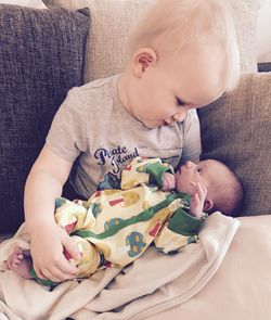 High angle view of brother with newborn sister sitting on sofa at home