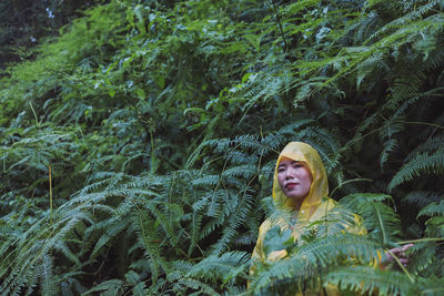 Portrait of woman in raincoat standing against plants