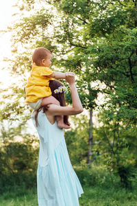 Woman carrying baby on shoulders against plants