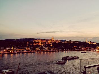 Scenic view of river by buildings against sky at sunset