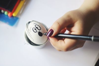 Cropped hand of woman drawing on egg at table