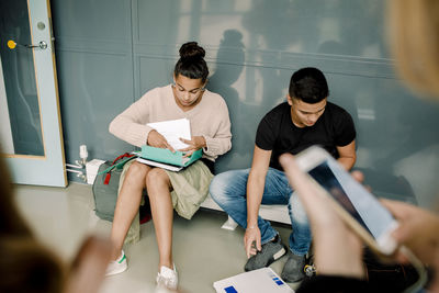 Male and female students completing homework while sitting in school corridor