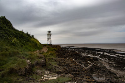 Lighthouse amidst sea and buildings against sky