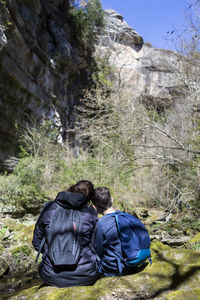 Back view of two young teenagers sitting on river shore