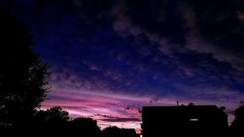 Low angle view of silhouette trees and buildings against sky at sunset