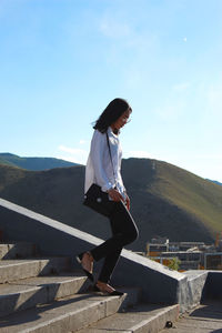 Side view of woman standing on mountain against sky