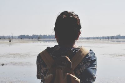 Rear view of woman with backpack standing at beach against sky