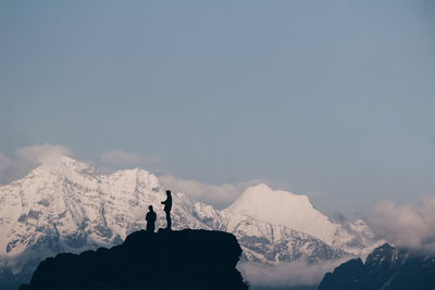 Silhouette person standing on snowcapped mountain against sky