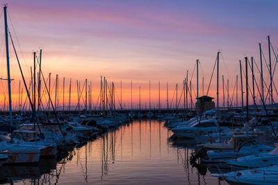 Sailboats moored in harbor at sunset