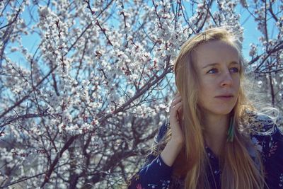 Young woman looking away against cherry blossom tree