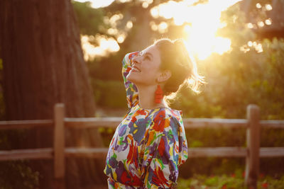 Woman looking away while standing against trees