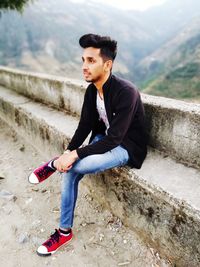 Young man looking away while sitting on mountain