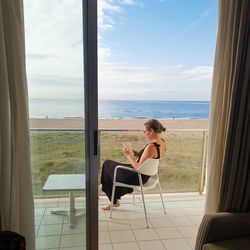 Woman reading book while sitting on chair seen through window
