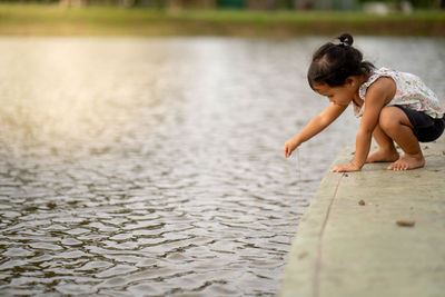 Cute girl putting stone into lake