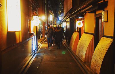 Rear view of people walking in illuminated city at night