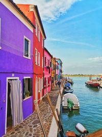 Boats moored in sea by houses against sky