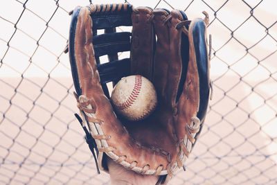 Close-up of baseball in glove against chainlink fence