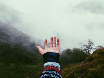 Close-up of man hand on mountain against sky