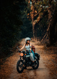 Young woman sitting on motorcycle in forest