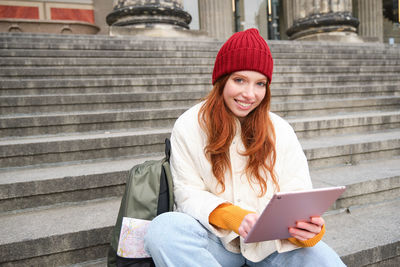 Young woman using digital tablet while sitting on staircase