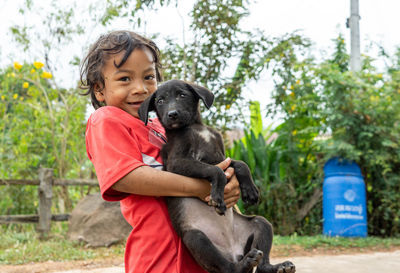 A girl in rural thailand, holding a dog along the road, teasing each other, dog, cute