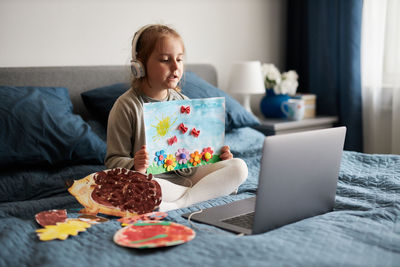 Little girl preschooler learning online showing her works drawings done at home