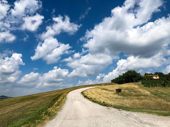 Dirt road amidst field against sky