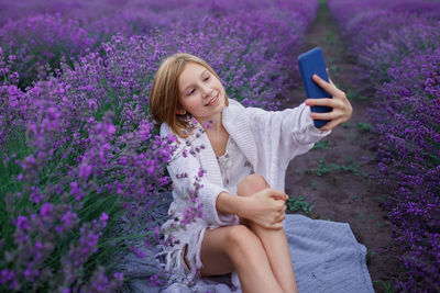 Cute girl taking selfie sitting against lavender farm