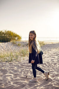 Portrait of a girl with long hair run on a sandy beach in a black leather jacket