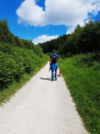 Rear view of hiker walking with dog on road against sky
