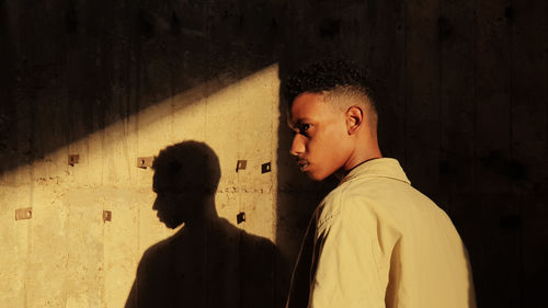 Side view of young man standing against wall