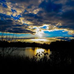 Silhouette of trees and lake against cloudy sky