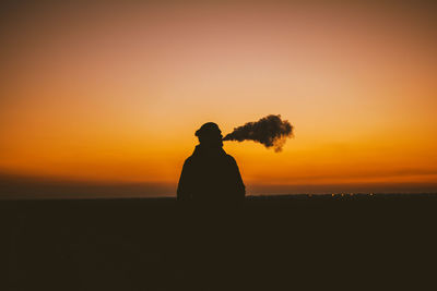 Silhouette man standing against orange sky during sunset