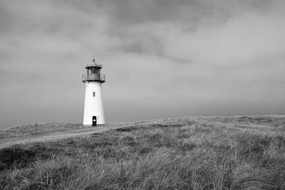 Lighthouse on field by building against sky