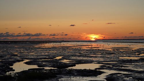 Scenic view of low tide at sea against sky during sunset