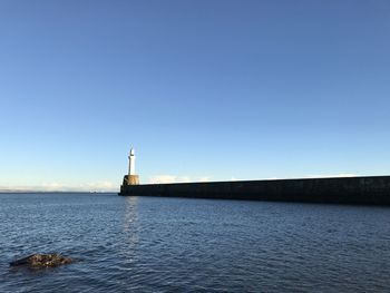 Lighthouse by sea against clear blue sky