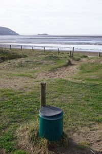 Wooden post on field by sea against sky