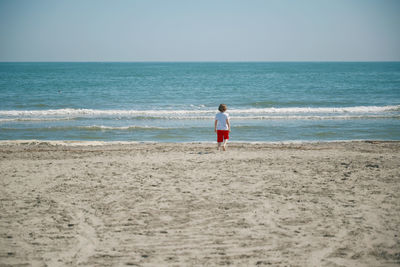 Rear view of a child standing on beach against sky