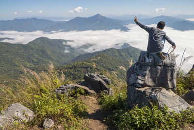 Man sitting on the cliff and looking at the valley and mountains in the daylight