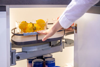 Hand pushes modern pull-out shelf with lemons  in kitchen cupboard 