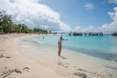 Side view of young woman in bikini standing at beach against sky