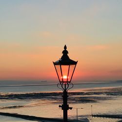 Silhouette street light on beach against sky during sunset