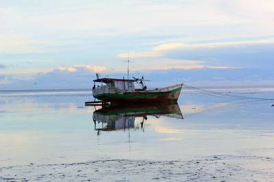 Fishing boat moored at sea against sky during sunset