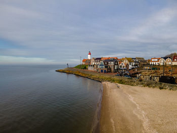 Lighthouse amidst sea and buildings against sky