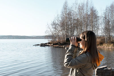 Young woman looking through binoculars at birds on lake birdwatching, ecology research autumn